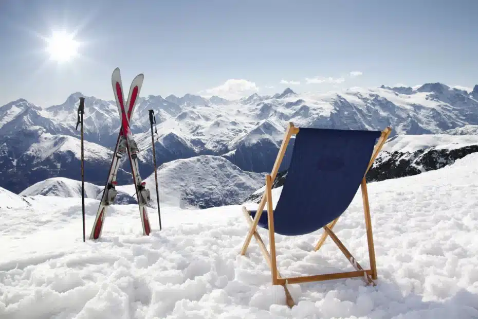 Klappstuhl im Schnee neben aufgestellten Skiern in der Sonne mit Blick auf Berggipfel im Winterurlaub